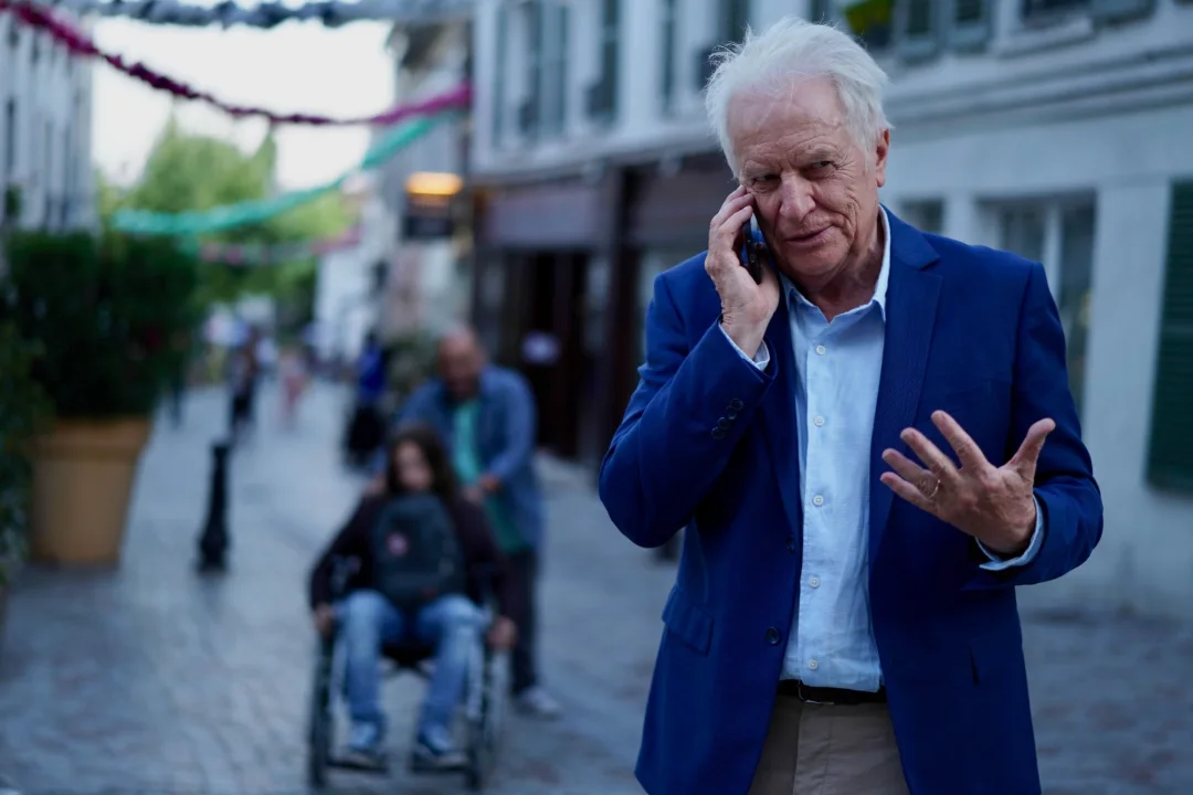 Un homme aux cheveux blancs téléphone dans une rue animée.