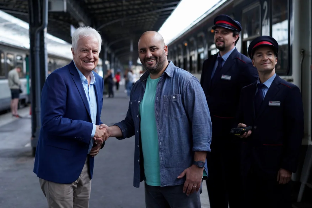 Sur un quai de gare, deux hommes se serrent la main devant deux contrôleurs.