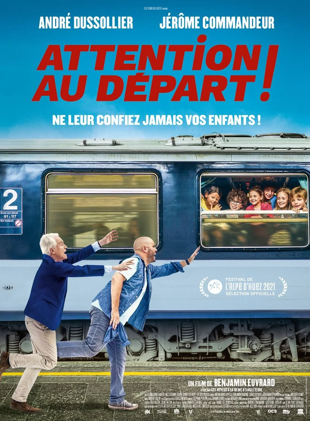 Affiche d'Attention au départ ! avec André Dussollier et Jérôme Commandeur : deux hommes courent sur un quai devant un train rempli d'enfants.