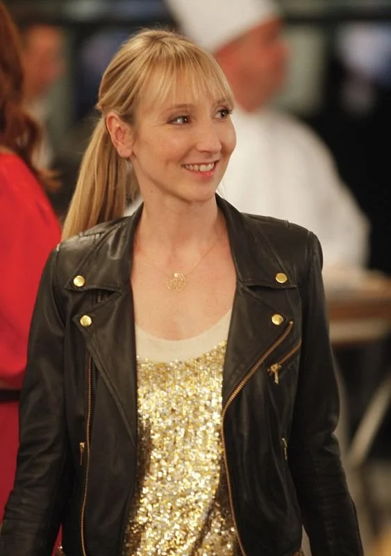 Une femme blonde en veste de cuir et haut doré, au milieu d'une fête.