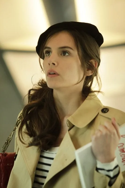 Une jeune femme en béret et trench-coat.
