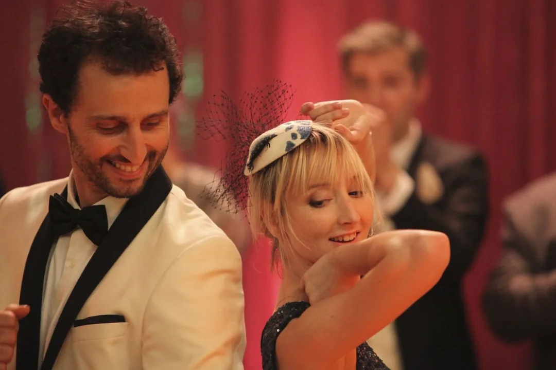 Un homme en smoking blanc et une invitée blonde rient pendant la soirée.