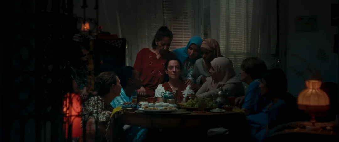 Une famille réunie autour d'une table dans un intérieur sombre éclairé par des lampes.