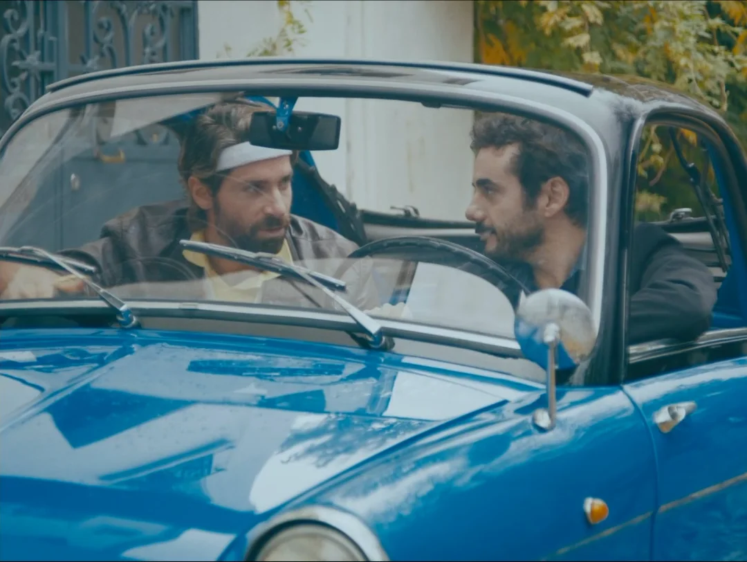 Deux hommes à bord d'un cabriolet bleu.